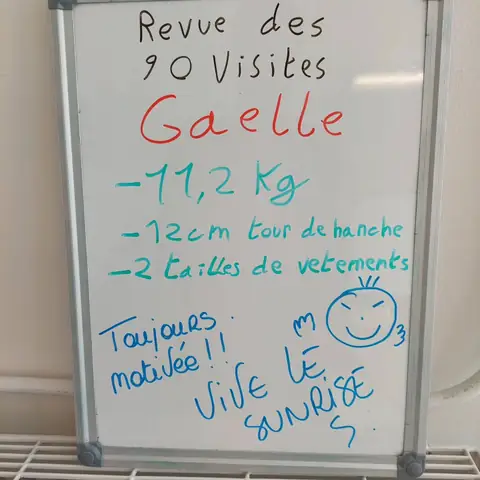 Dans la salle, une membre pose avec son bilan noté sur une ardoise blanche