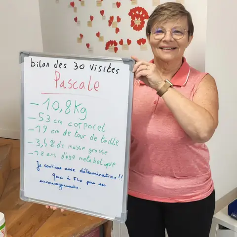 Dans la salle, une membre pose avec son bilan noté sur une ardoise blanche