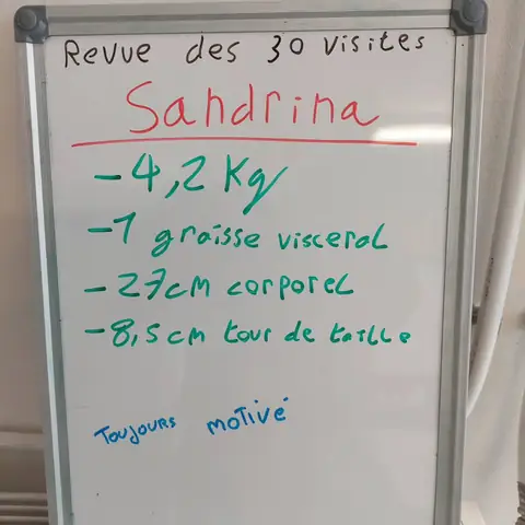 Dans la salle, une membre pose avec son bilan noté sur une ardoise blanche