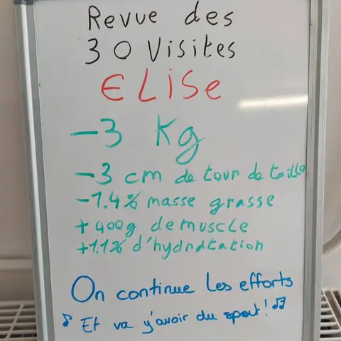 Dans la salle, une membre pose avec son bilan noté sur une ardoise blanche