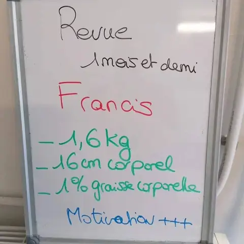 Dans la salle, un membre pose avec son bilan noté sur une ardoise blanche