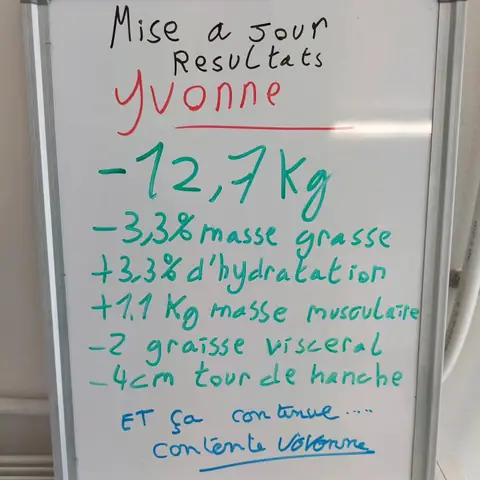 Dans la salle, une membre pose avec son bilan noté sur une ardoise blanche