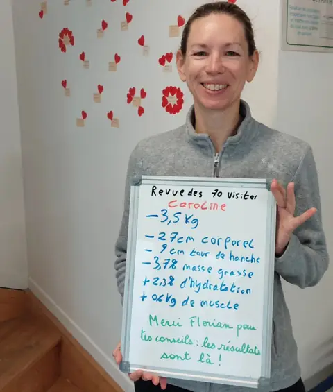 Dans la salle, une membre pose avec son bilan noté sur une ardoise blanche