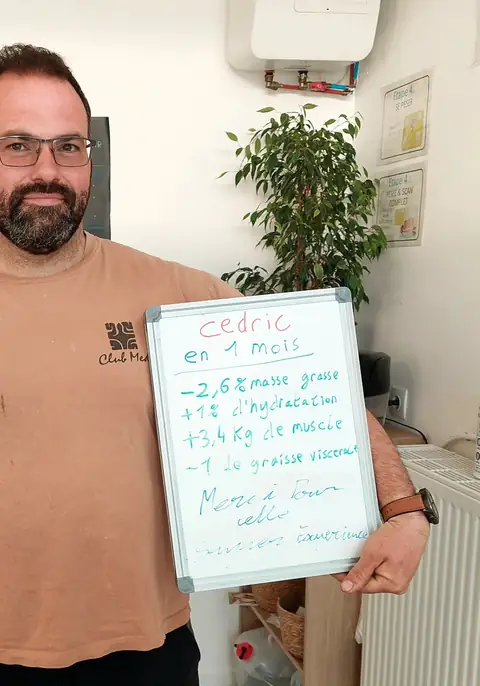 Dans la salle, un membre pose avec son bilan noté sur une ardoise blanche