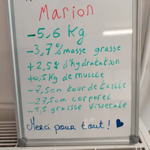 Dans la salle, une membre pose avec son bilan noté sur une ardoise blanche